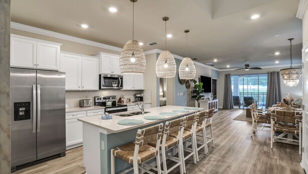 A modern kitchen with stainless steel appliances, a central island with bar stools, and pendant lighting. - Coastal Haven | 7BR, Custom Built Kids Rooms, Arcade, Private Pool (Davenport)