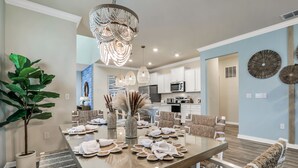 A modern dining area with a glass table, white chairs, and a chandelier. - Coastal Haven | 7BR, Custom Built Kids Rooms, Arcade, Private Pool (Davenport)