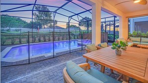 A covered outdoor area with a pool, seating, and a view of the landscape. - Coastal Haven | 7BR, Custom Built Kids Rooms, Arcade, Private Pool (Davenport)