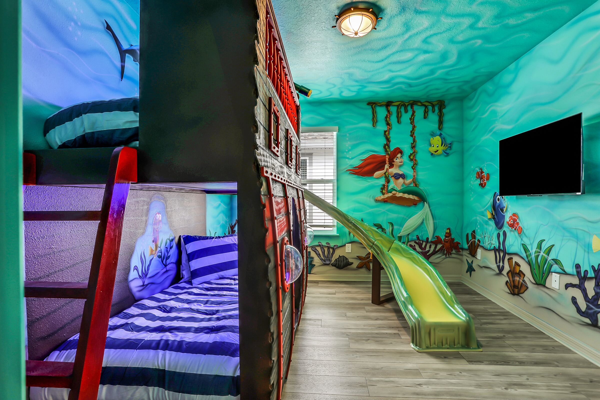 A room with a bunk bed, a slide, and a mural of an underwater scene.