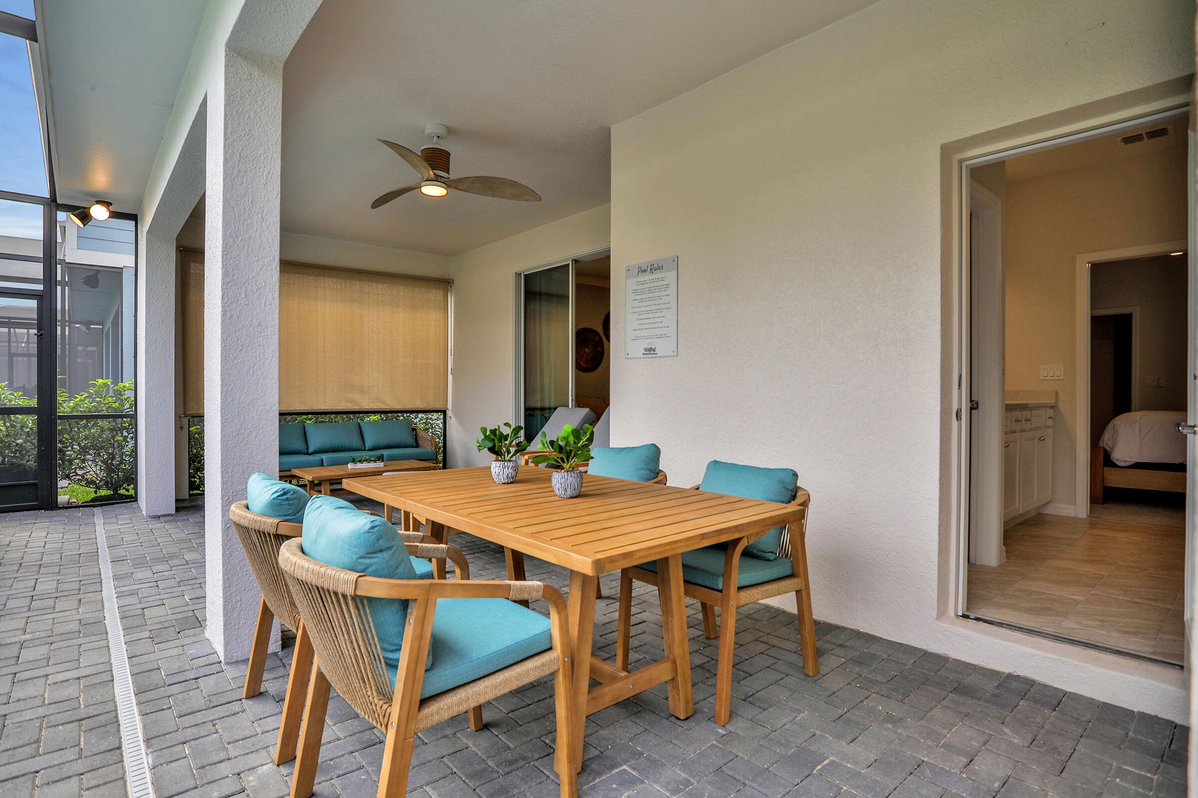 A covered patio area with a wooden table and chairs, a ceiling fan, and a view into the house.