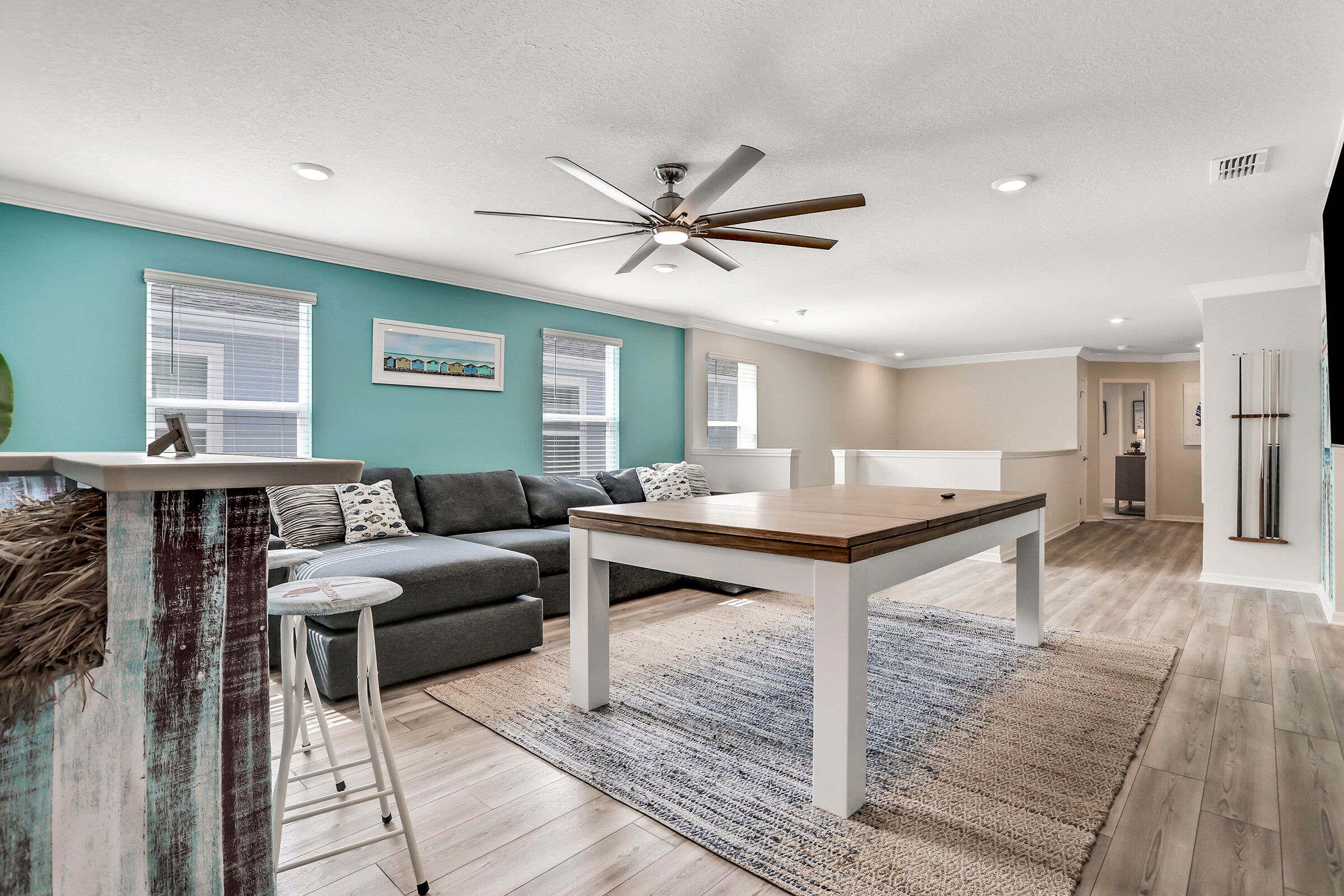 A modern living room with a dining table, a sofa, and a ceiling fan.