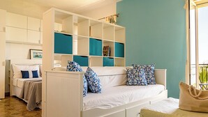 Un dormitorio con un sofá blanco, una cama con almohadas azules y blancas, un armario blanco y una pared verde azulado.