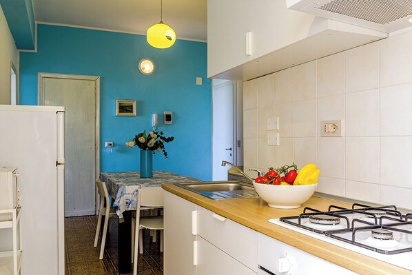 A kitchen with a blue wall, white cabinets, a wooden countertop, a gas stove, and a sink.