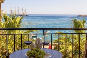 A balcony with a table set for two, overlooking a coastal area with ships and boats.