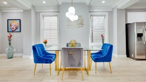 A modern dining area with a glass table, blue velvet chairs, and a chandelier.