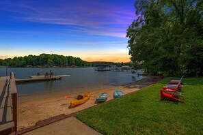 A lakeside view with a dock, kayaks, and a grassy area.