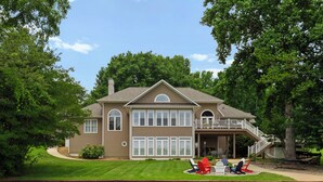 A two-story house with a covered porch, a landscaped lawn, and a sandy beach area. - Keepin' It Cooley by SoCharm | Lake Norman! (Mooresville)
