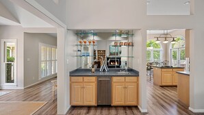 A spacious kitchen with wooden cabinets, a built-in dishwasher, and a central island. There are glass shelves above the island displaying various items. - Keepin' It Cooley by SoCharm | Lake Norman! (Mooresville)
