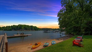 A lakeside dock with kayaks and paddleboards, a wooden pier, and a grassy area with benches. - Keepin' It Cooley by SoCharm | Lake Norman! (Mooresville)