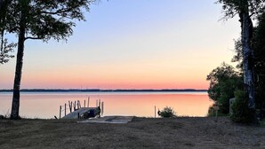Vista panorámica de un lago con un muelle de madera que se adentra en aguas tranquilas, rodeado de árboles y una zona verde.