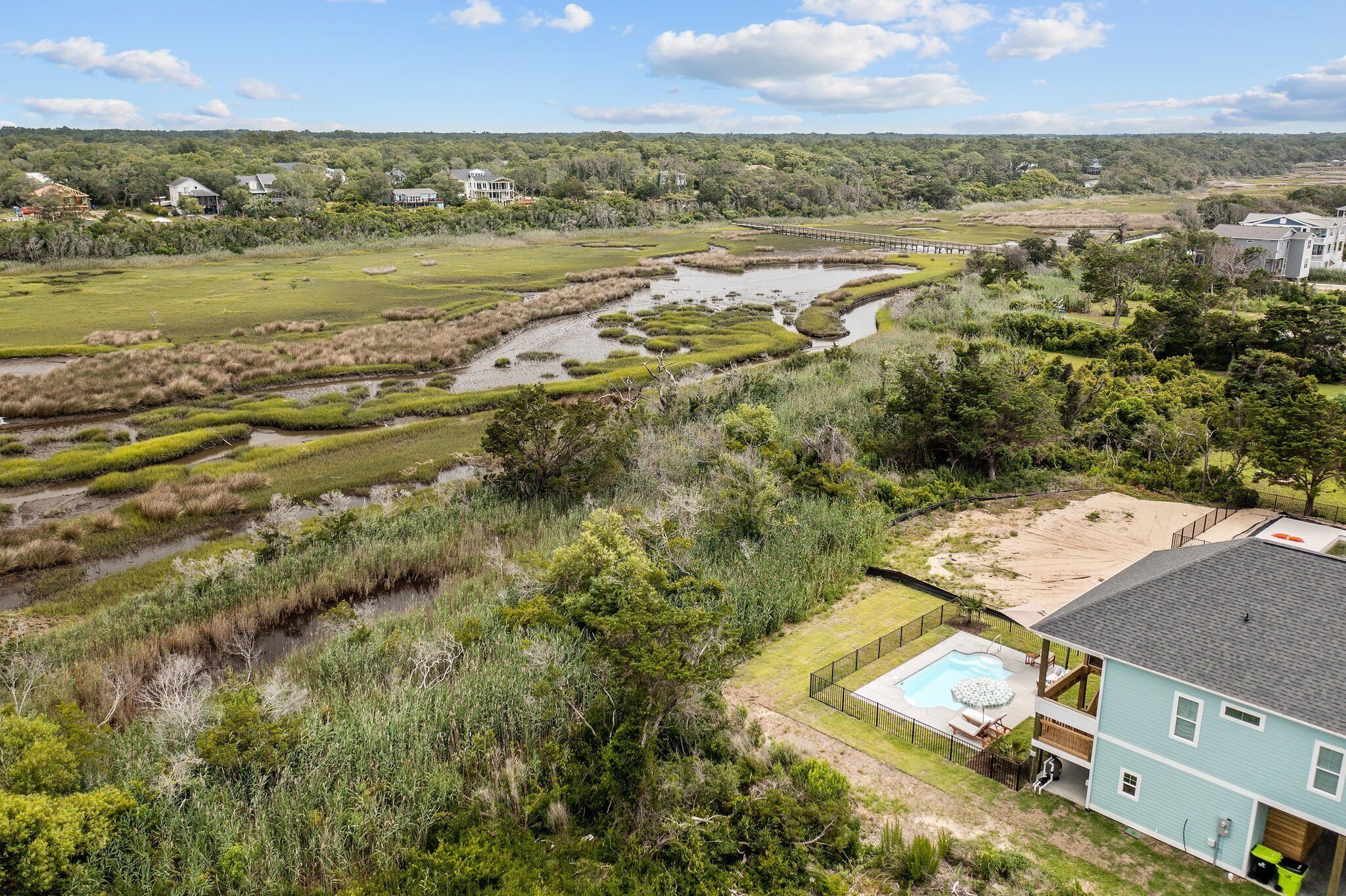 A residential area with a swimming pool, a large house, and a marshy landscape.