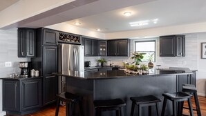 Una cocina moderna con armarios oscuros, un refrigerador de acero inoxidable, una isla central con taburetes y un ventanal que proporciona luz natural.