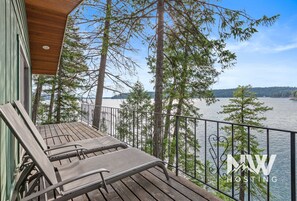 A wooden deck with two lounge chairs overlooking a lake, surrounded by trees and a metal railing. - Waterfront Cabin—Private Dock with Boat Slip, Paddle Board for Fun on the Water! (Hayden)