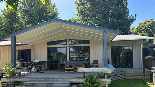 Una casa moderna con un porche cubierto, mobiliario exterior y vistas al entorno verde.