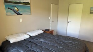Un dormitorio con una cama grande, una mesita de noche, un cuadro en la pared y una puerta.