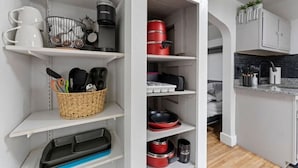 A kitchen with white cabinets, a countertop, and various kitchen items like pots, pans, and utensils.