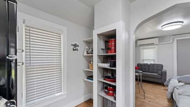 A compact living space with a kitchenette, a coffee bar sign, and a grey sofa.