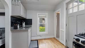 A compact kitchen with white cabinets, a black countertop, a window, and a stove.