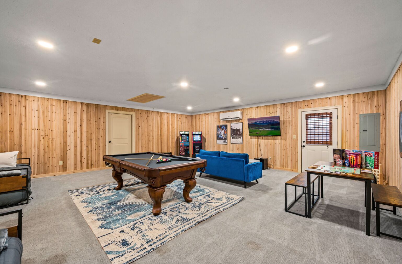 A room with a pool table, blue sofa, and gaming consoles.