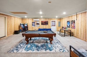 Une pièce avec une table de billard, un canapé bleu et un mur en bois orné de tableaux.