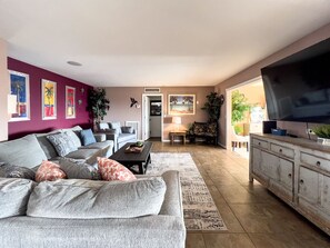 Relax in this stylish living room with a sofa, coffee table, and TV, surrounded by artwork and lush greenery.