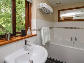 A bathroom with a sink, a bathtub, a window with a view of greenery, and a towel rack with towels. - Nant Glas (Llanwrda)