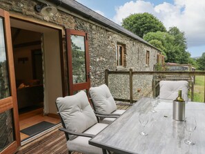 A rustic stone building with a wooden deck, outdoor seating, and a view of the countryside. - Nant Glas (Llanwrda)
