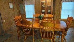 A wooden dining table with six chairs, a cabinet with glass doors, and a window with blinds. - Cozy Bear Rock Cottage with hot tub  (Monroe)