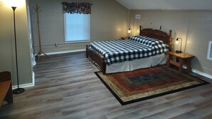 A bedroom with a bed, a nightstand, a lamp, a floor lamp, a window with blinds, and a radiator. - Cozy Bear Rock Cottage with hot tub  (Monroe)