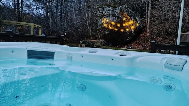 A hot tub with a view of a forested area and a rock illuminated by lights. - Cozy Bear Rock Cottage with hot tub  (Monroe)