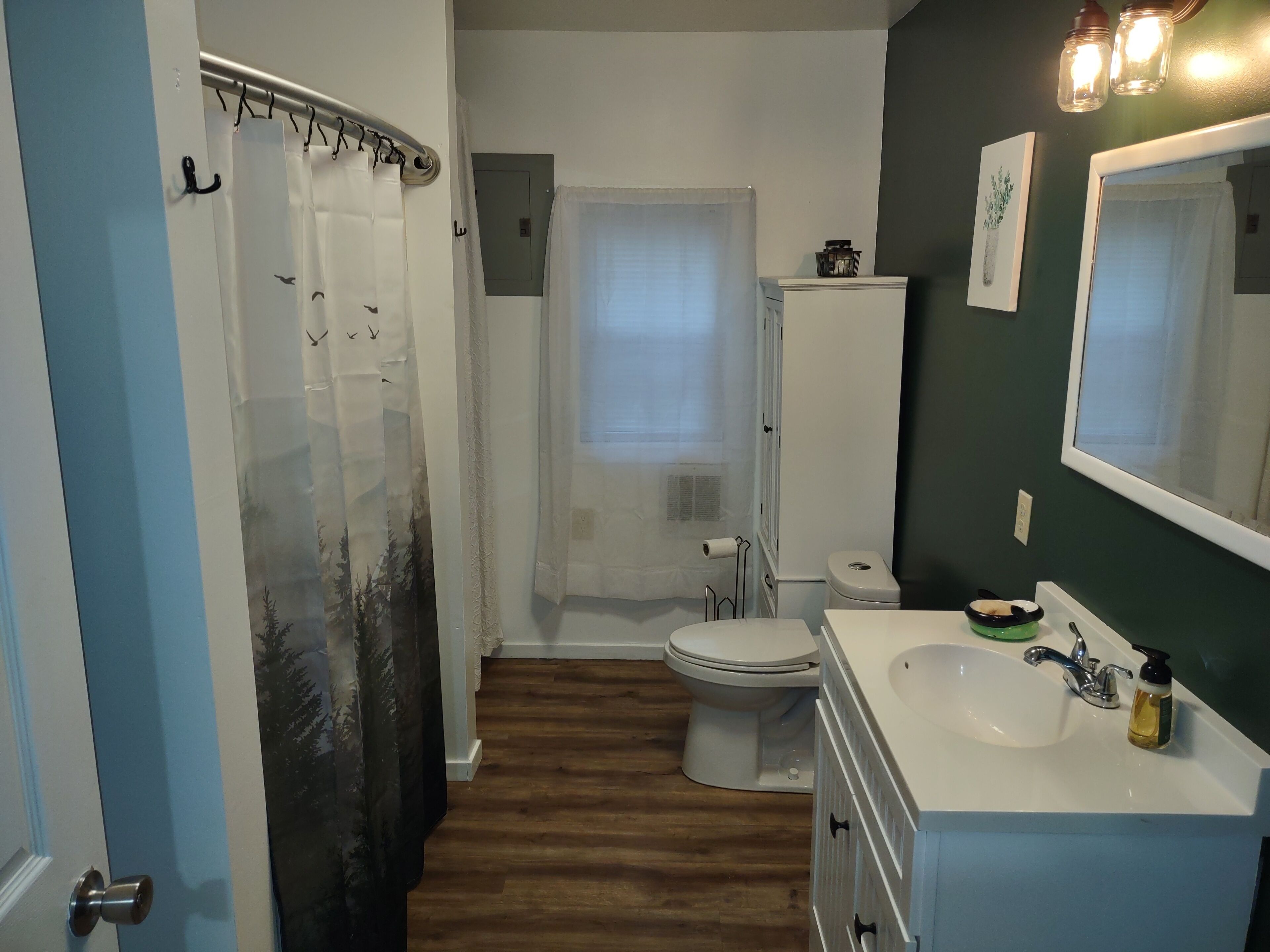 A bathroom with a shower curtain, toilet, sink, and mirror.