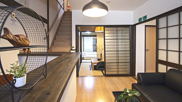 Ein modernes Interieur mit einem hölzernen Empfangsschalter, einem schwarzen Ledersofa, einer hängenden Pendelleuchte und einer Treppe.