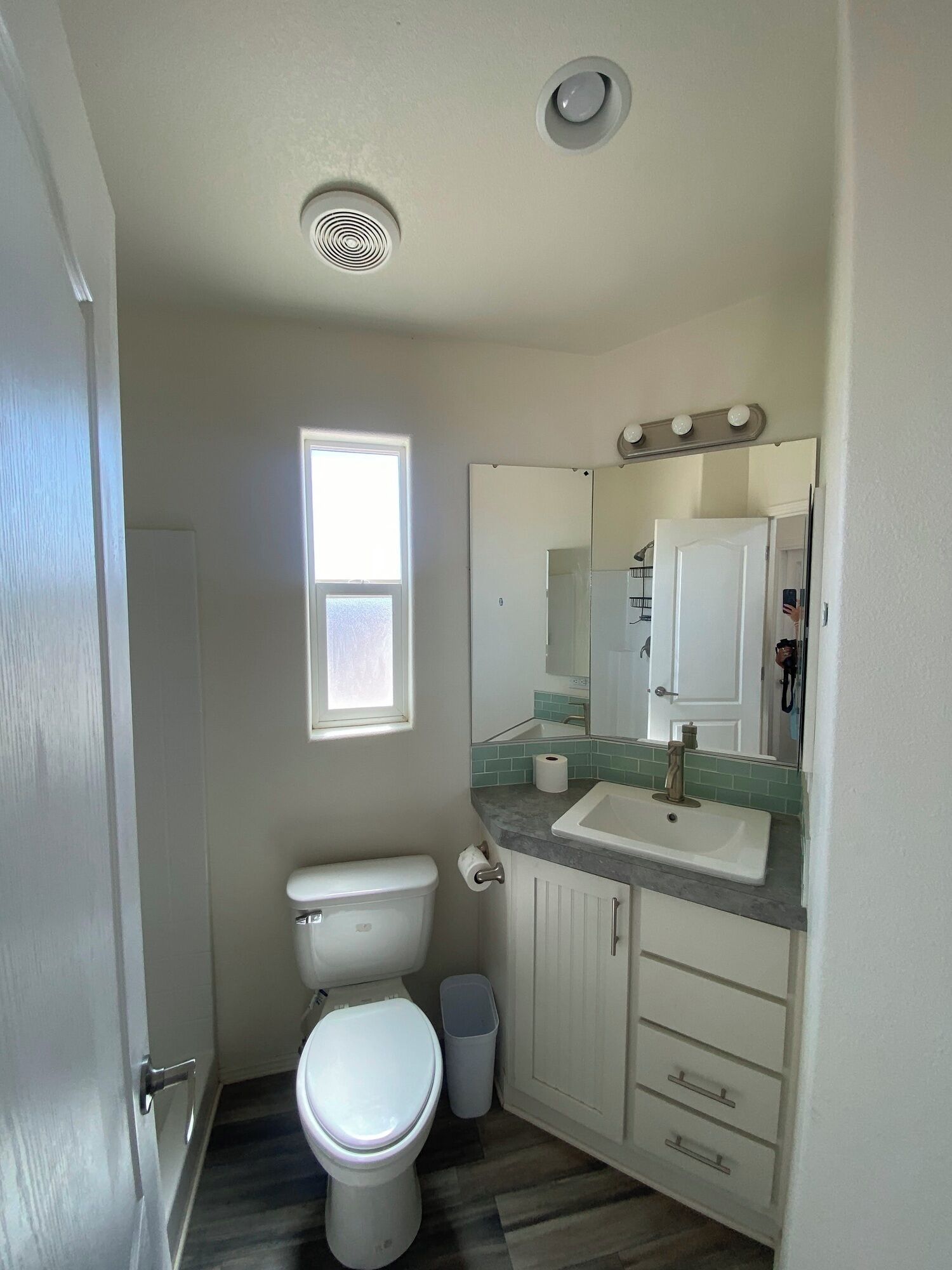A small, clean bathroom with a toilet, sink, mirror, and a window.