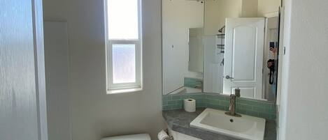 A small, clean bathroom with a toilet, sink, mirror, and a window.