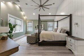 Ein Schlafzimmer mit einem Himmelbett, einem Nachttisch, einer Kommode, einem Deckenventilator und einem großen Fenster mit Jalousien.