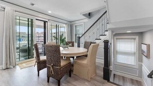 Un espace repas avec une table ronde et des chaises, un escalier et une vue à travers des portes vitrées.