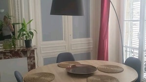 Un comedor con una mesa redonda, sillas azules, una lámpara de pie negra y un amplio ventanal con cortinas.