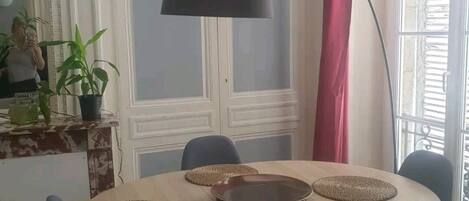Ein Essbereich mit einem runden Tisch, blauen Stühlen, einer schwarzen Stehlampe und einem großen Fenster mit Vorhängen.
