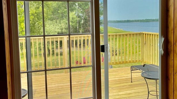 A bedroom with a large sliding glass door leading to a wooden deck with a view of a lake. -  Lakeside Hideaway: Full-Home Retreat on the Remote Boney Falls Basin (Cornell)