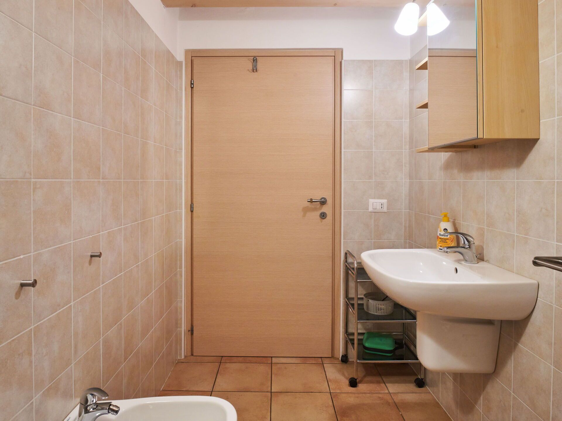 A bathroom with a wooden door, a white sink, and a mirror above it.