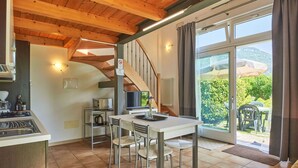 A kitchen with a stove, microwave, and sink, a dining area with a table and chairs, and a view of a garden through a sliding glass door.