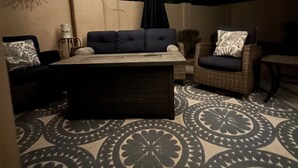 Un espace patio extérieur doté d’un ventilateur de plafond, de guirlandes lumineuses, d’un tapis à motifs et de mobilier d’extérieur comprenant un canapé et des fauteuils.