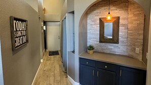 Un couloir avec une pancarte sur laquelle on peut lire « AUJOURD’HUI, ÇA VA ÊTRE UNE EXCELLENTE JOURNÉE », un plancher en bois, une armoire bleu foncé et un mur en pierre orné d’un miroir.