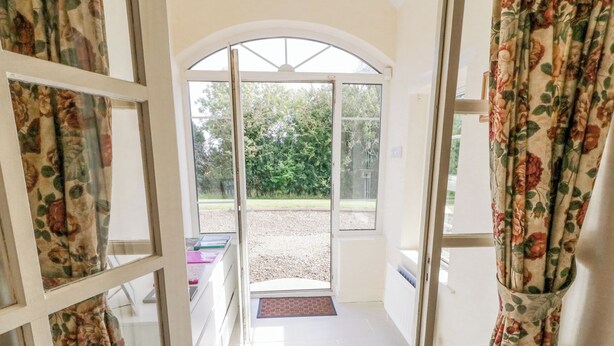 An open doorway leading to a covered outdoor area with a gravel path and greenery in the background. - Craiglea Cottage (Coleraine)