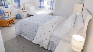 A bedroom with a large bed, a smaller bed, a chair, a bedside table, and a lamp. - Craiglea Cottage (Coleraine)