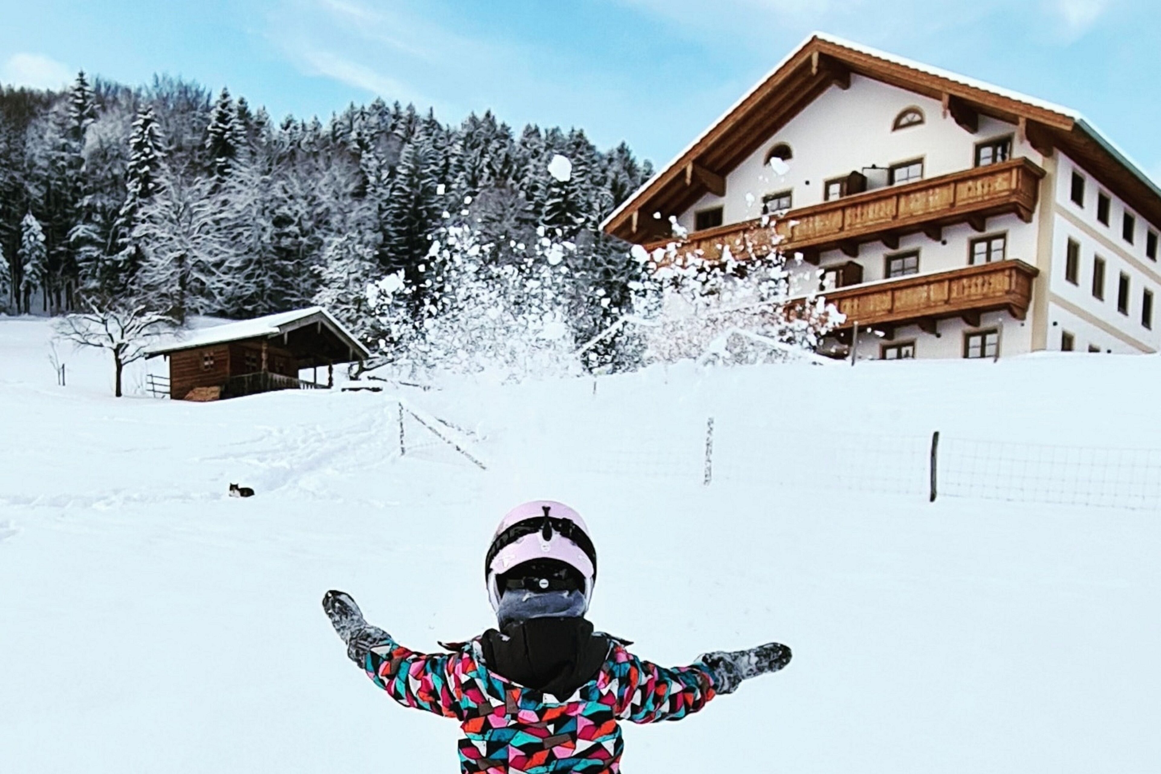 A snow-covered landscape with a wooden chalet and a multi-story building with balconies.