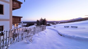 Schneebedeckte Landschaft mit einem Holzbau, einem verschneiten Zaun und Bänken.