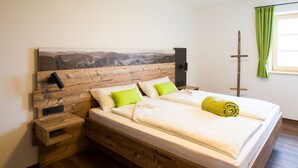 Ein Zimmer mit hölzernem Kopfteil, einem Bett mit weißer Bettwäsche und grünen Kissen, einem Nachttisch und einem grünen Vorhang.