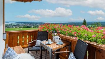 Eine Holzterrasse mit Tisch und Stühlen, die einen schönen Ausblick auf eine Landschaft mit Blumen und eine entfernte Ansicht von Häusern und Grünflächen bietet.